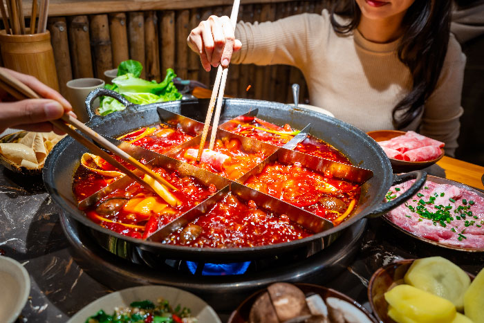Esta imagen ilustra la tradicional y popular experiencia gastronómica del Hot Pot de Chongqing (caldero o la olla caliente), un plato insignia de la cocina de Sichuan, China.