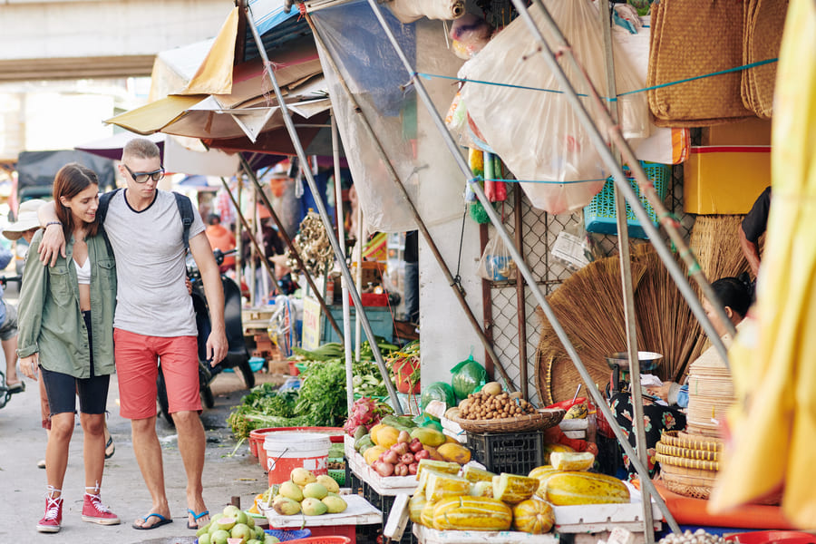Esta imagen muestra una escena cotidiana y espontánea en un concurrido mercado callejero al aire libre, situado en una localidad del sudeste asiático