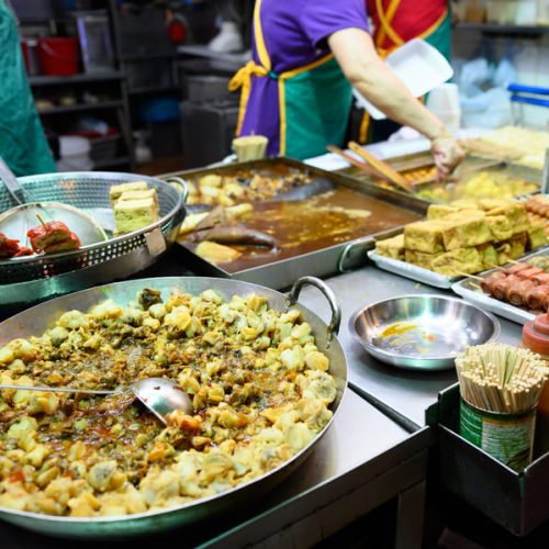 Una toma nocturna vibrante y llena de dinamismo que muestra un concurrido mercado callejero de comida en una urbe china.